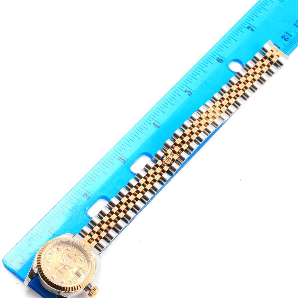The image shows a Rolex Datejust 179173 Women's Steel and Gold (two tone) Champagne Dial 179173 Women's Steel and Gold (two tone) Champagne Dial watch laid flat beside a ruler, highlighting its face and two-tone bracelet.