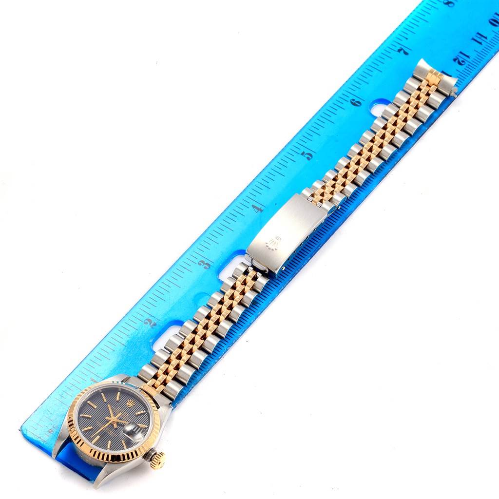 The Rolex Datejust 79173 Women's Steel and Gold (two tone) Black Dial 79173 Women's Steel and Gold (two tone) Black Dial watch is shown lying flat with a blue ruler beside it, displaying its face, band, and clasp.