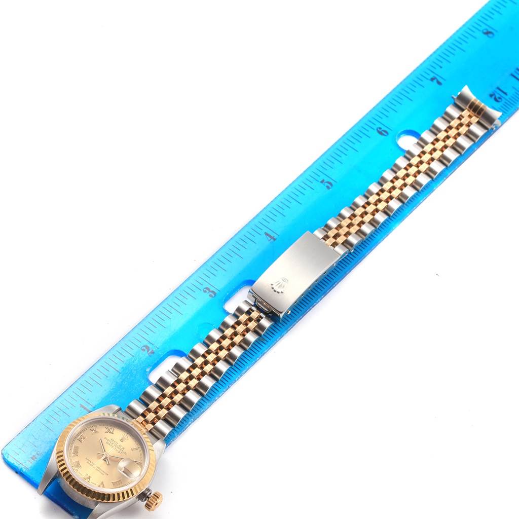 The image shows the Rolex Datejust 79173 Women's Steel and Gold (two tone) Champagne Dial 79173 Women's Steel and Gold (two tone) Champagne Dial watch alongside a blue ruler, highlighting the watch face, bezel, and two-tone bracelet.