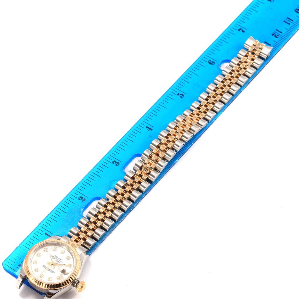 The image shows a Rolex Datejust 179173 Women's Steel and Gold (two tone) Mother of Pearl Dial 179173 Women's Steel and Gold (two tone) Mother of Pearl Dial watch laid flat against a blue ruler, highlighting its face and jubilee bracelet.