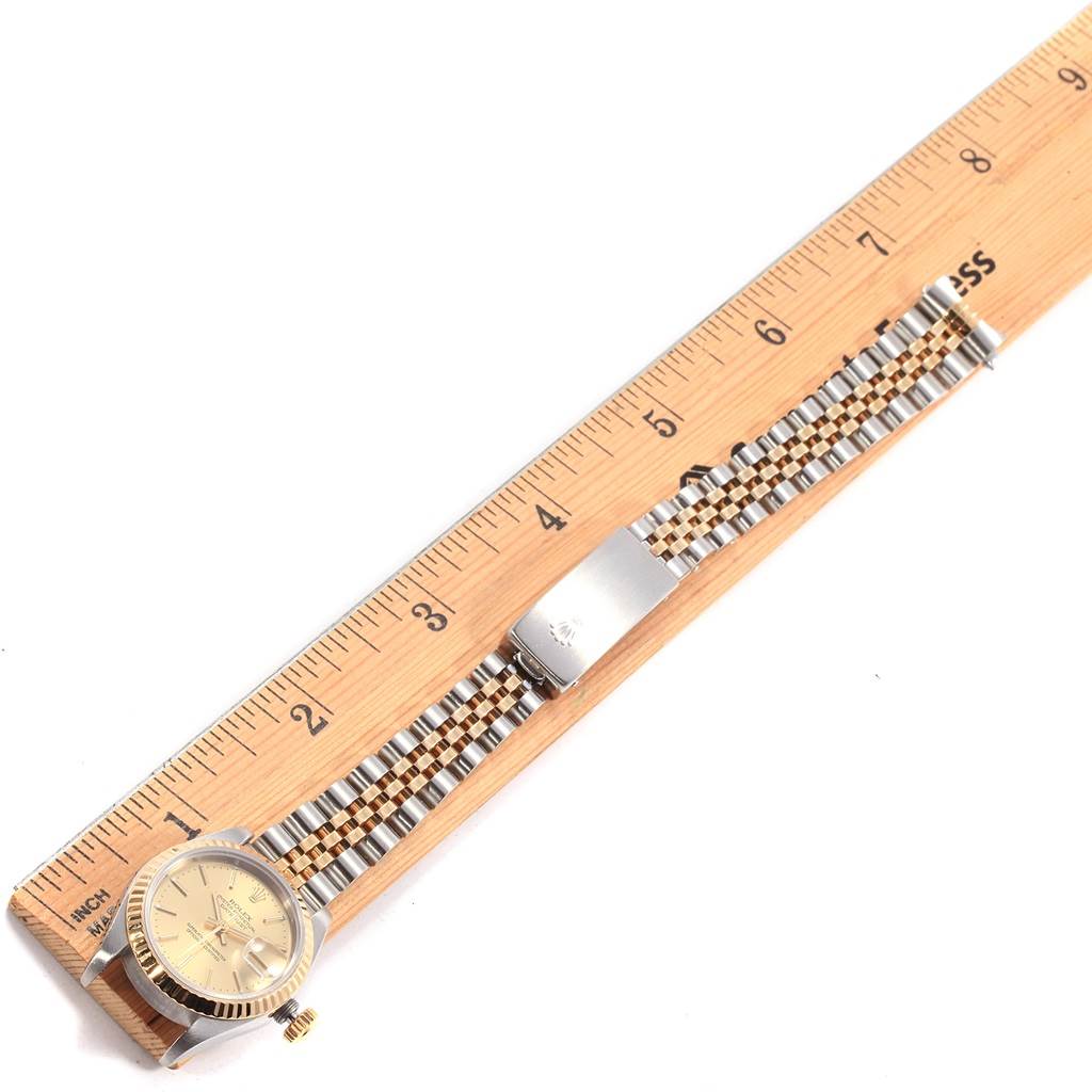 The Rolex Datejust 79173 Women's Steel and Gold (two tone) Champagne Dial 79173 Women's Steel and Gold (two tone) Champagne Dial watch is shown from a top-down angle with its band fully extended beside a ruler.