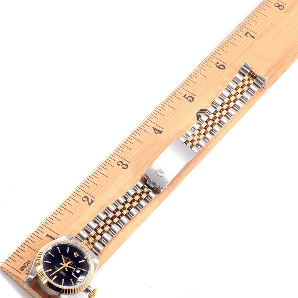 This image shows a Rolex Datejust 79173 Women's Stainless Steel Black Dial 79173 Women's Stainless Steel Black Dial watch laid flat next to a wooden ruler, showcasing its face, bracelet, and clasp.