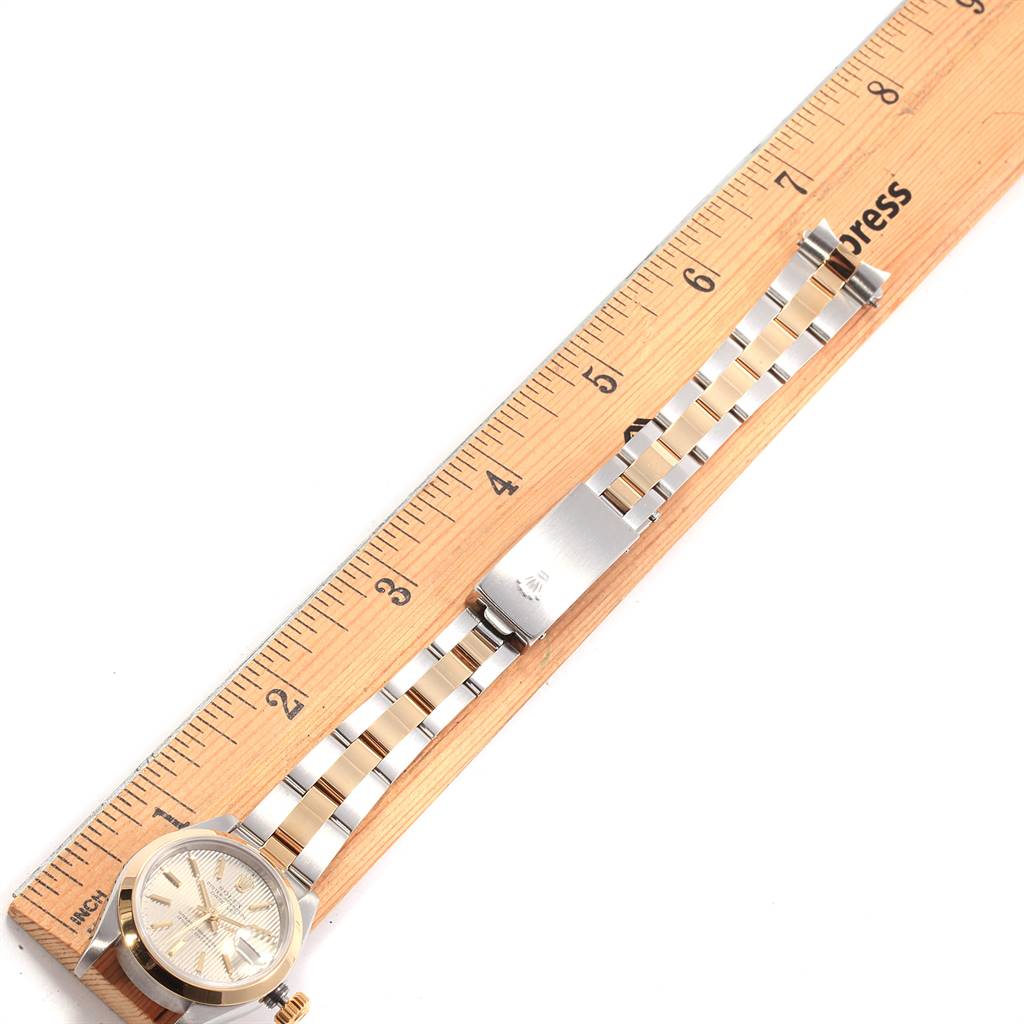 The Rolex Datejust 79163 Women's Steel and Gold (two tone) Silver Dial 79163 Women's Steel and Gold (two tone) Silver Dial watch is shown from a top-down angle, displaying its bracelet and clasp alongside a wooden ruler.