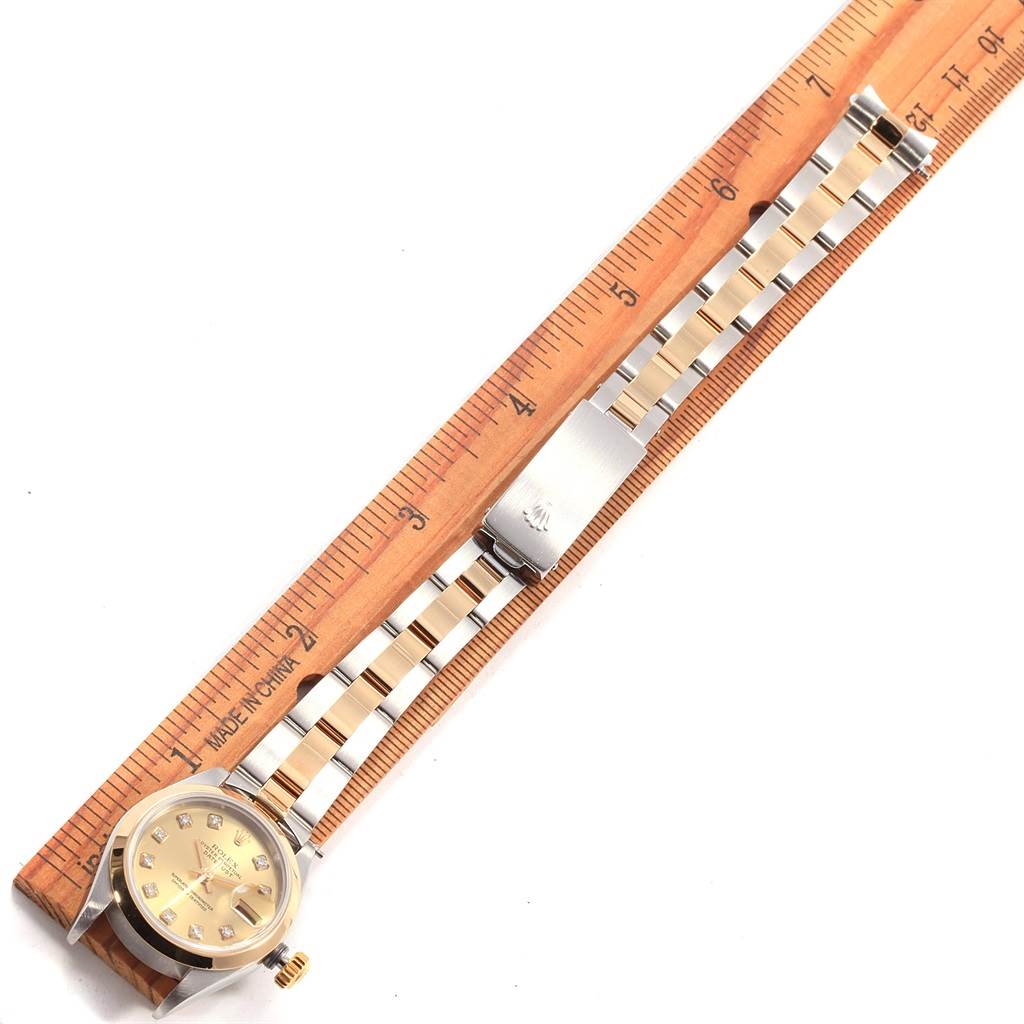 This image shows a Rolex Datejust 79163 Women's Steel and Gold (two tone) Champagne Dial 79163 Women's Steel and Gold (two tone) Champagne Dial watch, face down, with its gold and silver bracelet extended and measured next to a wooden ruler.