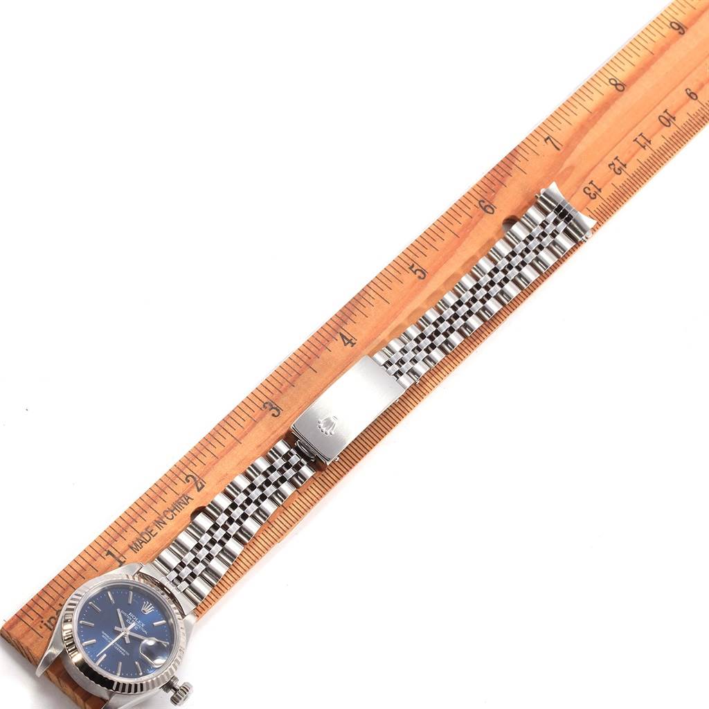 The image shows a top view of a Rolex Datejust 69174 Women's Stainless Steel Blue Dial 69174 Women's Stainless Steel Blue Dial watch with a blue dial and a stainless steel Jubilee bracelet, next to a wooden ruler.
