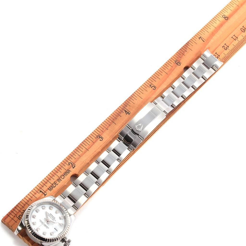 The image shows the Rolex Datejust 179174 Women
s Stainless Steel White Dial 179174 Women
s Stainless Steel White Dial watch laid flat with a wooden ruler, displaying the watch face, bracelet, and clasp from a top-down angle.