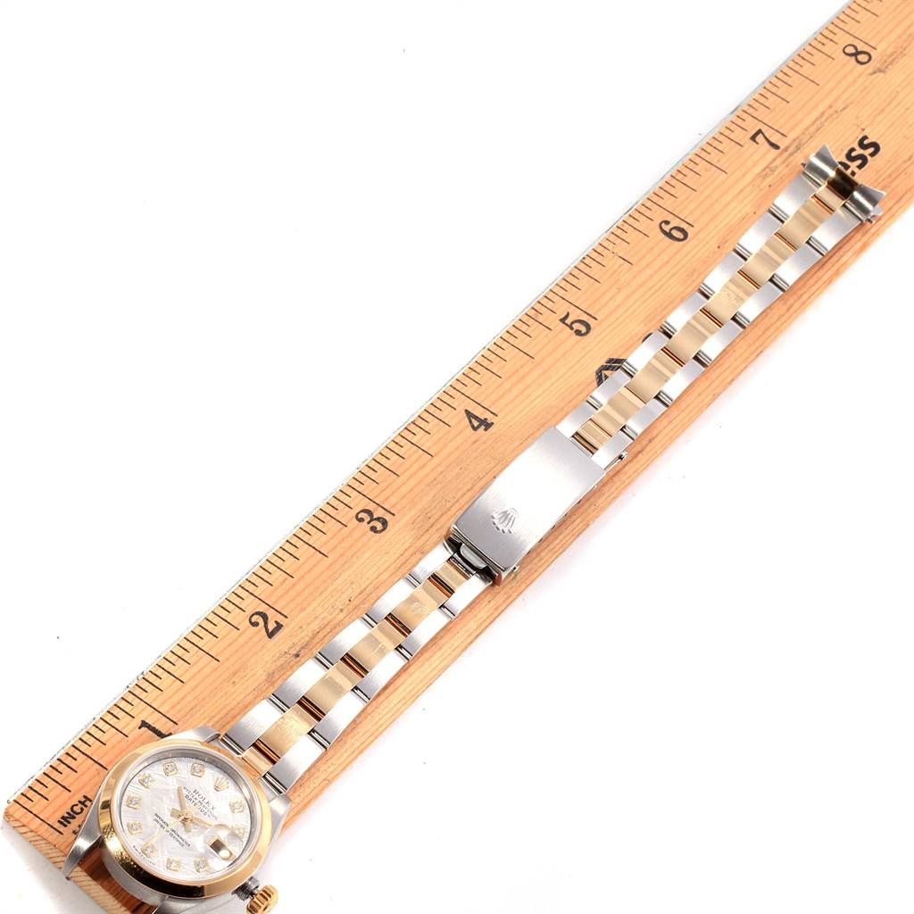 This image shows a Rolex Datejust 79163 Women's Steel and Gold (two tone) Silver Dial 79163 Women's Steel and Gold (two tone) Silver Dial watch laid flat on a wooden ruler, displaying the face, strap, and clasp.