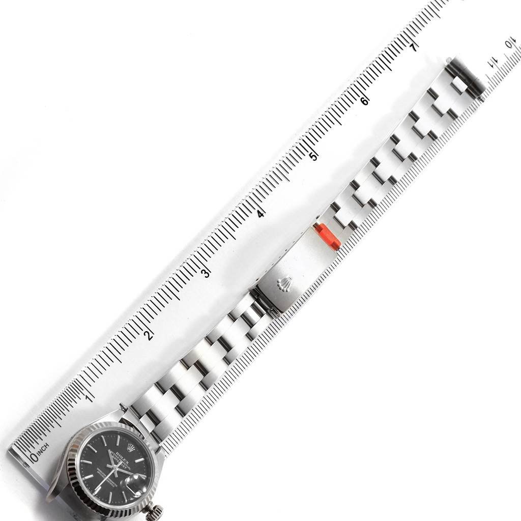 The Rolex Datejust 79174 Women's Stainless Steel Black Dial 79174 Women's Stainless Steel Black Dial watch in the image is shown vertically with the face, bracelet, and a ruler for size reference.