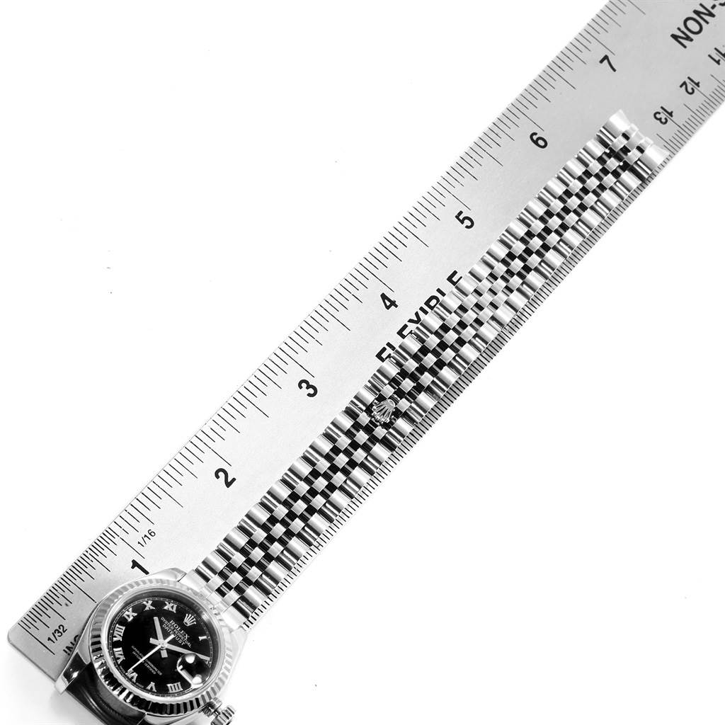The image shows the Rolex Datejust 179174 Women's Stainless Steel Black Dial 179174 Women's Stainless Steel Black Dial watch face and partial band next to a ruler, viewed from an overhead angle.