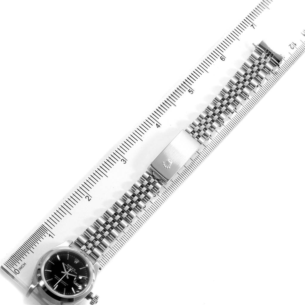 This image shows the Rolex Datejust 69160 Women's Stainless Steel Black Dial 69160 Women's Stainless Steel Black Dial watch at a slight diagonal angle, featuring its dial, bracelet, and clasp next to a ruler for scale.