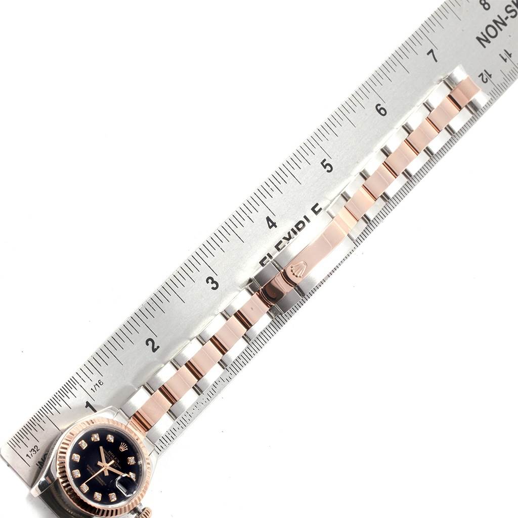 The image shows a Rolex Datejust 179171 Women's Steel and Gold (two tone) Black Dial 179171 Women's Steel and Gold (two tone) Black Dial watch laid flat next to a ruler, displaying its strap and face.