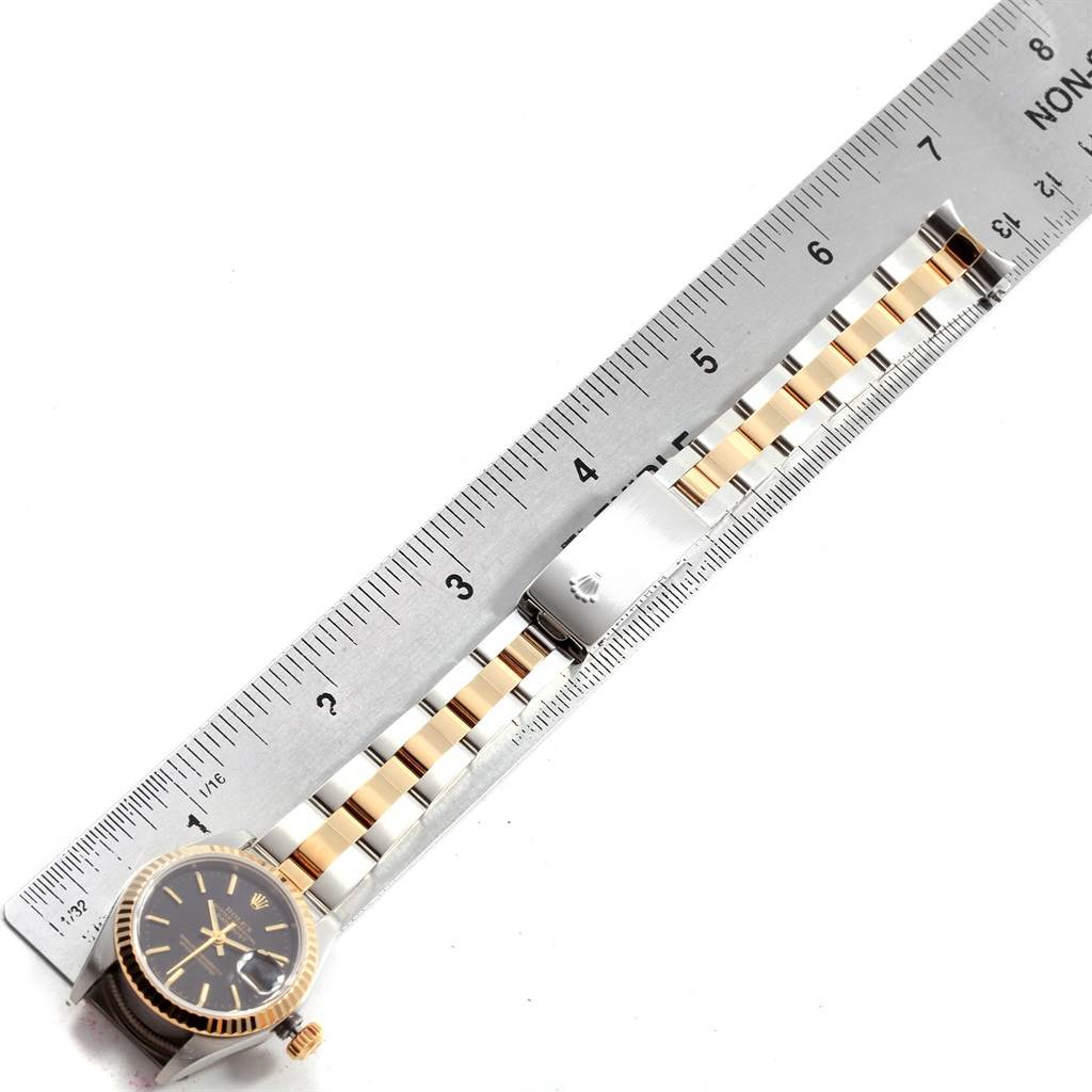 The image shows a Rolex Datejust 79173 Women
s Stainless Steel Black Dial 79173 Women
s Stainless Steel Black Dial watch laid flat with the face, bezel, and bracelet alongside a ruler.