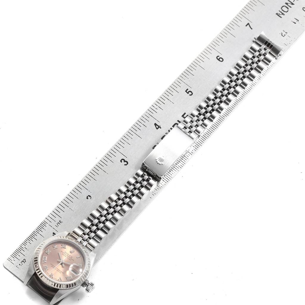 The image shows a Rolex Datejust 79174 Women
s Stainless Steel Pink Dial 79174 Women
s Stainless Steel Pink Dial watch from a top view, highlighting the watch face and metal bracelet next to a ruler.