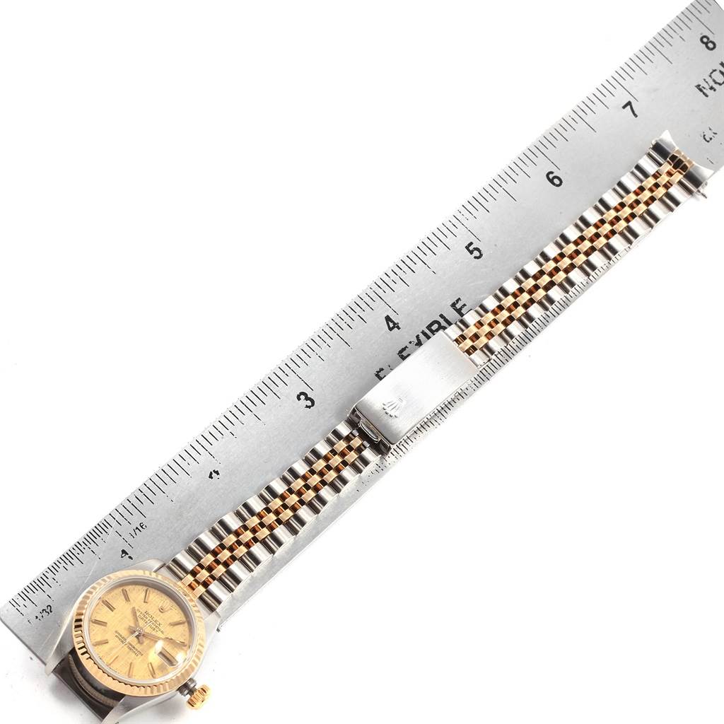 This image shows a top-down view of a Rolex Datejust 69173 Women
s Stainless Steel Champagne Dial 69173 Women
s Stainless Steel Champagne Dial watch with its band and clasp alongside a ruler for scale.