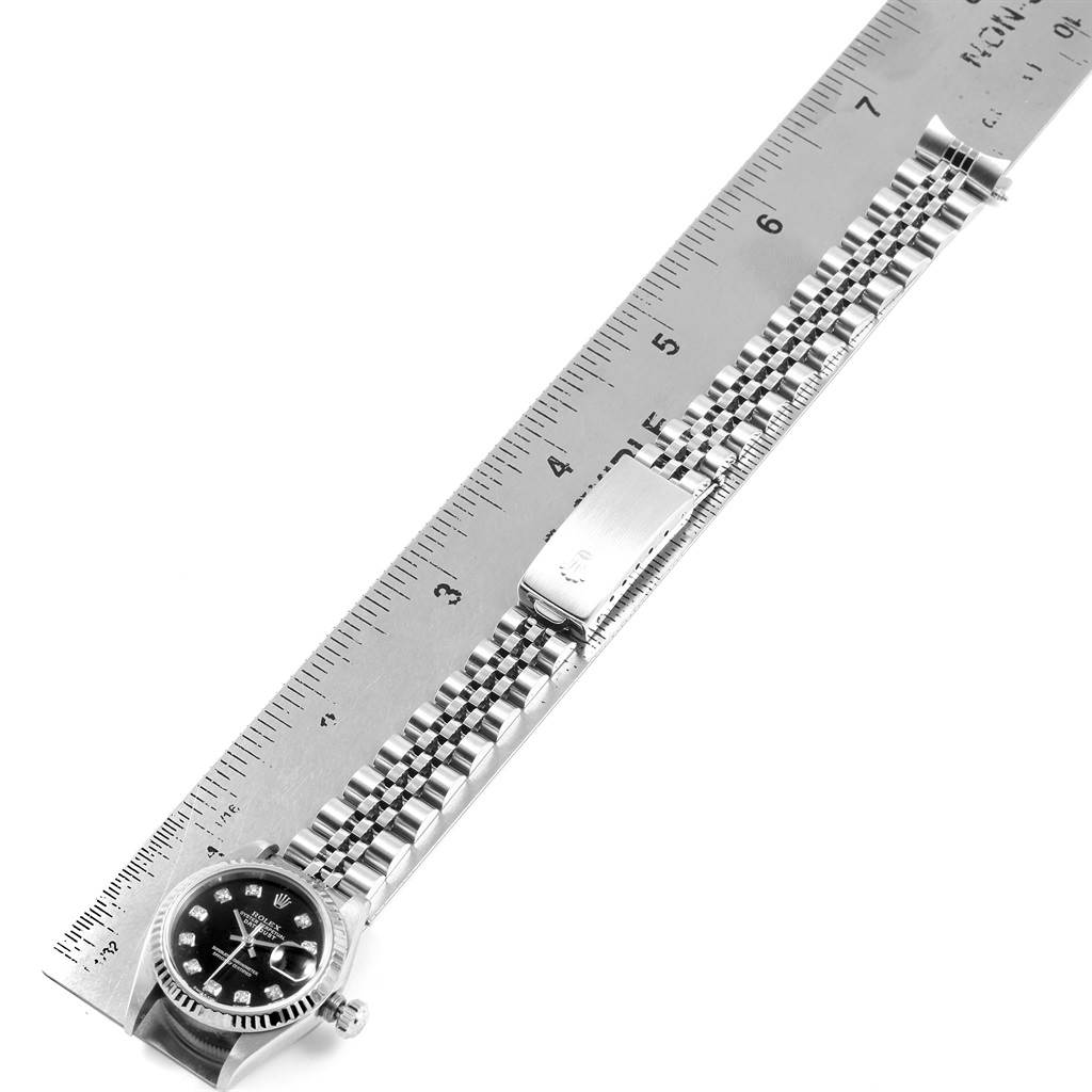 The Rolex Datejust 79174 Women's Stainless Steel Black Dial 79174 Women's Stainless Steel Black Dial watch is shown from a top-down angle, displaying the face, crown, and entire bracelet alongside a ruler for scale.