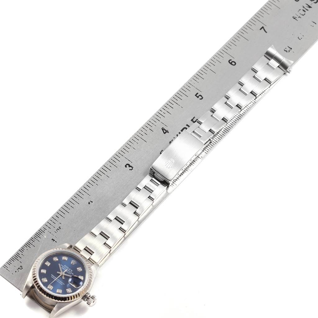 The Rolex Datejust 79174 Women
s Stainless Steel Blue Dial 79174 Women
s Stainless Steel Blue Dial watch is shown from an overhead angle, displaying the face, crown, bracelet, and clasp next to a ruler.