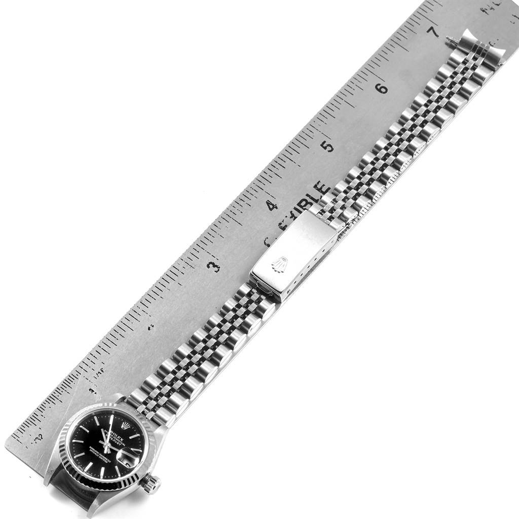 This image shows a Rolex Datejust 79174 Women's Stainless Steel Black Dial 79174 Women's Stainless Steel Black Dial watch laid flat, with the face and strap alongside a ruler for measurement.