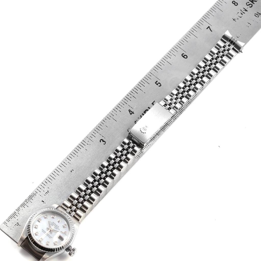 This image shows a Rolex Datejust 79174 Women
s Stainless Steel Mother of Pearl Dial 79174 Women
s Stainless Steel Mother of Pearl Dial watch laying flat against a ruler, displaying its face, bracelet, and clasp.