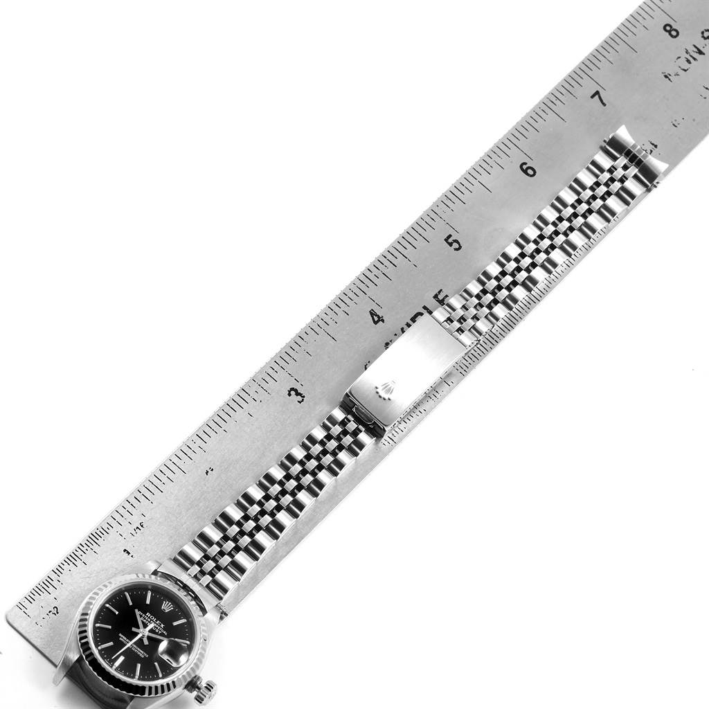 The image shows a Rolex Datejust 79174 Women
s Stainless Steel Black Dial 79174 Women
s Stainless Steel Black Dial watch laid flat alongside a ruler, focusing on the watch head and its metal bracelet.