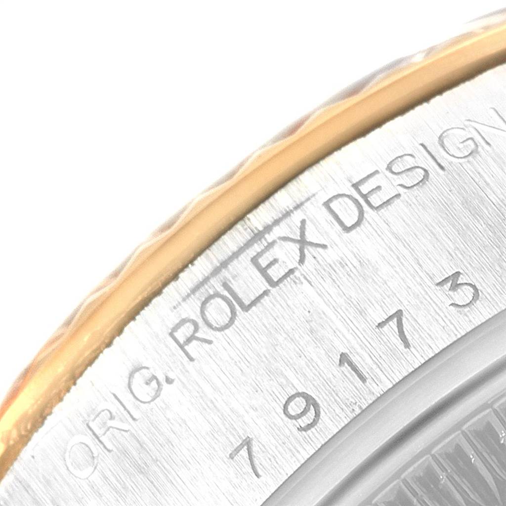 The image focuses on the engraved edge of a Rolex Datejust 79173 Women's Steel and Gold (two tone) Black Dial 79173 Women's Steel and Gold (two tone) Black Dial's back, displaying text and numbers in close-up detail.