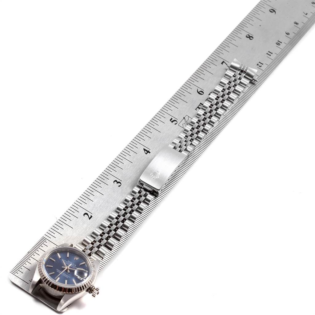 The image shows a Rolex Datejust 69174 Women
s Stainless Steel Blue Dial 69174 Women
s Stainless Steel Blue Dial model watch from a top-down angle, featuring the face and bracelet laid out along a ruler.