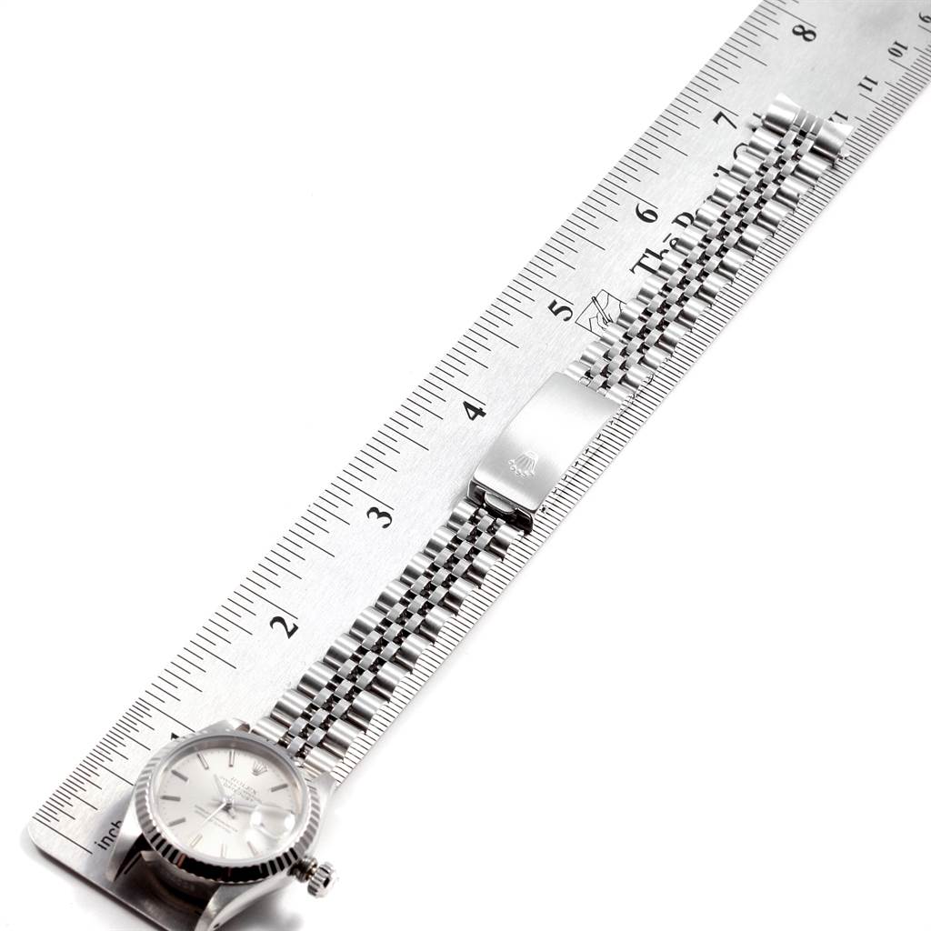 The image shows the Rolex Datejust 69174 Women
s Stainless Steel Silver Dial 69174 Women
s Stainless Steel Silver Dial watch laying on a ruler, displaying its face, bezel, and bracelet in a top-down angle.