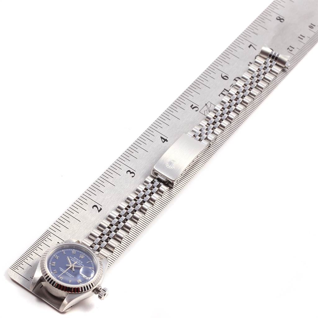 The image shows a top-down view of a Rolex Datejust 69174 Women
s Stainless Steel Blue Dial 69174 Women
s Stainless Steel Blue Dial watch laid alongside a metal ruler, highlighting its face, bezel, and bracelet.