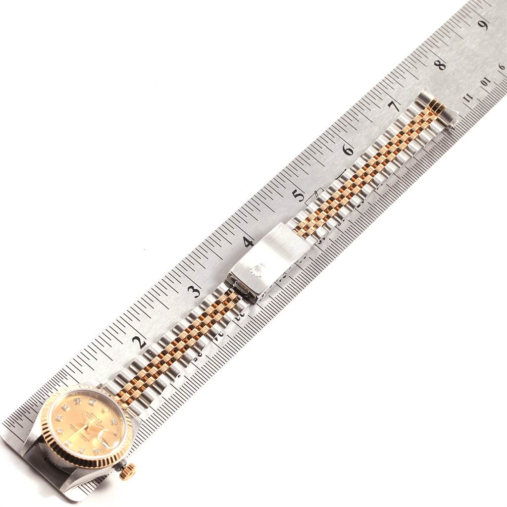 The image shows a Rolex Datejust 79173 Women
s Stainless Steel Champagne Dial 79173 Women
s Stainless Steel Champagne Dial watch with a gold dial and a two-tone band, aligned parallel to a ruler.