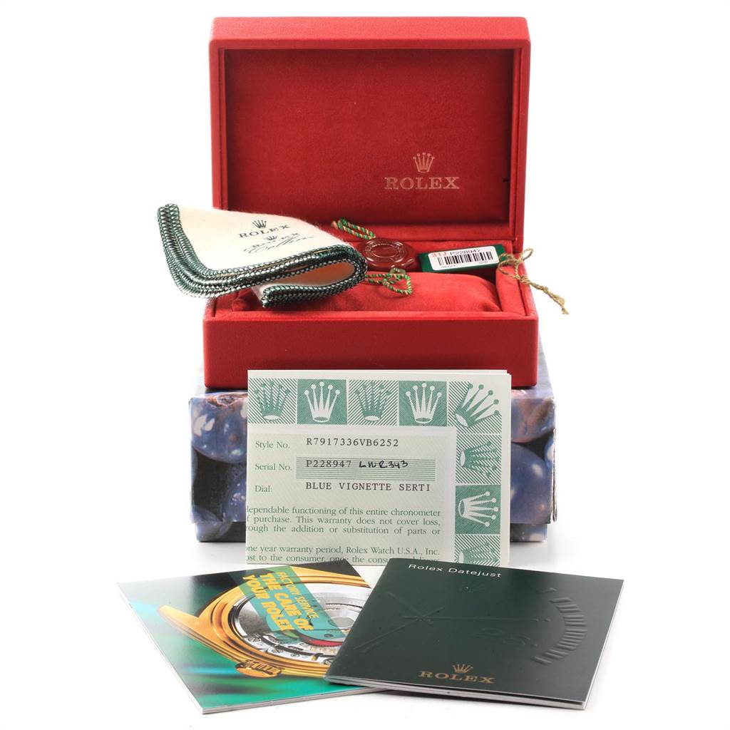The image shows a Rolex Datejust 79173 Women's Steel and Gold (two tone) Blue Dial 79173 Women's Steel and Gold (two tone) Blue Dial watch's red box, booklet, cleaning cloth, and warranty card from a frontal angle.