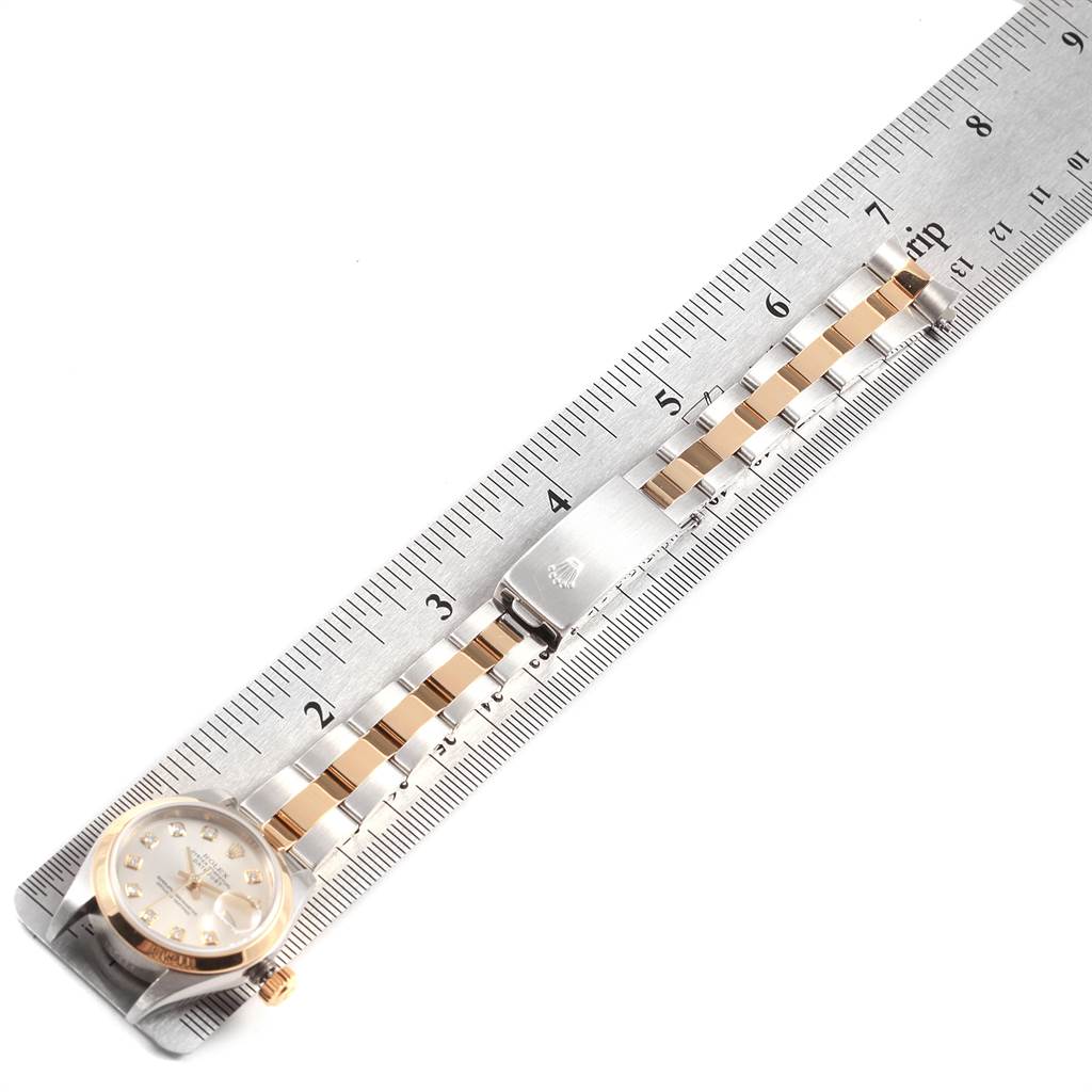 The Rolex Datejust 79163 Women's Steel and Gold (two tone) Silver Dial 79163 Women's Steel and Gold (two tone) Silver Dial watch is shown from a top angle, highlighting the face, bracelet, and clasp placed on a ruler.