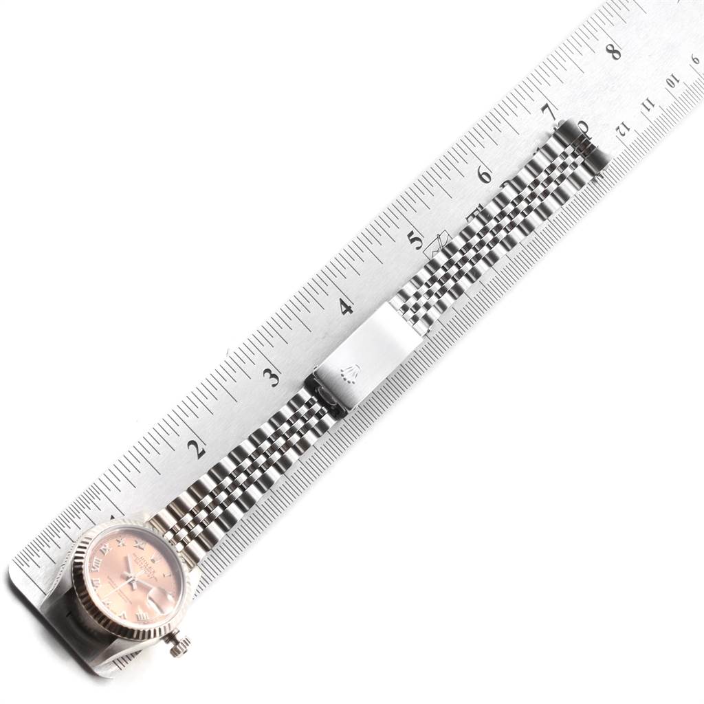 The Rolex Datejust 69174 Women's Stainless Steel Pink Dial 69174 Women's Stainless Steel Pink Dial watch is shown from a top-down angle, highlighting its dial, crown, and bracelet placed alongside a ruler.