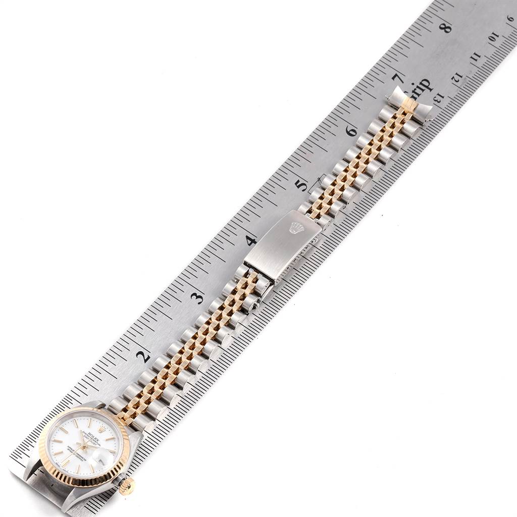 This image shows a Rolex Datejust 79173 Women
s Steel and Gold (two tone) White Dial 79173 Women
s Steel and Gold (two tone) White Dial watch laid flat beside a ruler, highlighting its bracelet and clasp.