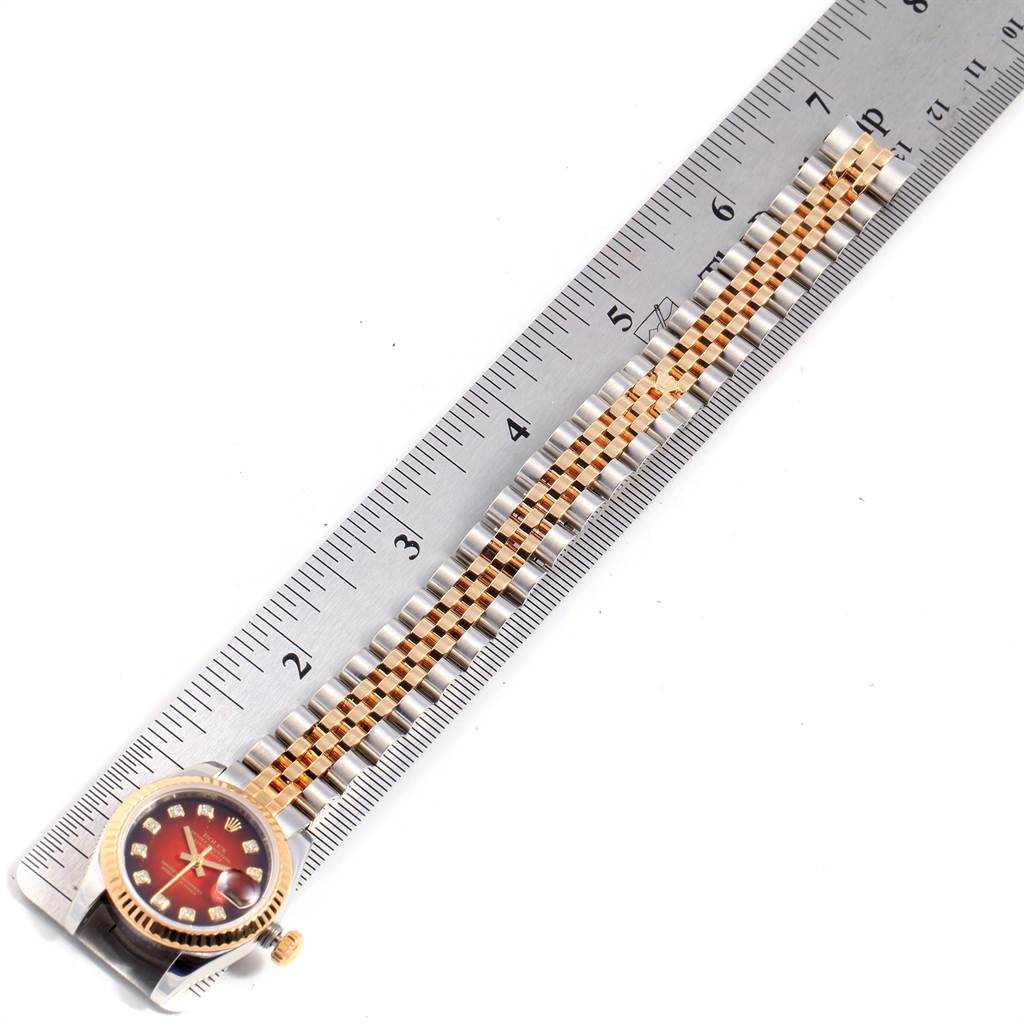 The Rolex Datejust 179173 Women
s Steel and Gold (two tone) Red Dial 179173 Women
s Steel and Gold (two tone) Red Dial watch is shown from an overhead angle, highlighting its face, crown, and bracelet against a ruler.