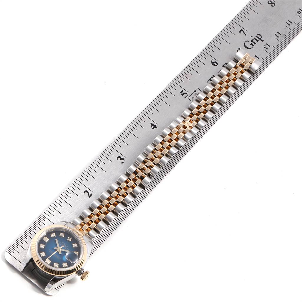 This image shows a Rolex Datejust 179173 Women
s Steel and Gold (two tone) Blue Dial 179173 Women
s Steel and Gold (two tone) Blue Dial watch taken at a top-down angle, highlighting its face, bezel, and partially extended band alongside a ruler.
