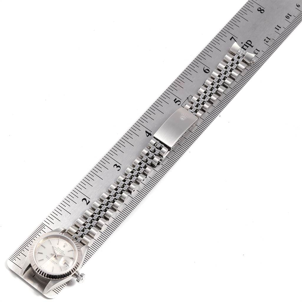 The image shows a Rolex Datejust 79174 Women
s Stainless Steel Silver Dial 79174 Women
s Stainless Steel Silver Dial watch and a part of its bracelet, aligned next to a ruler.
