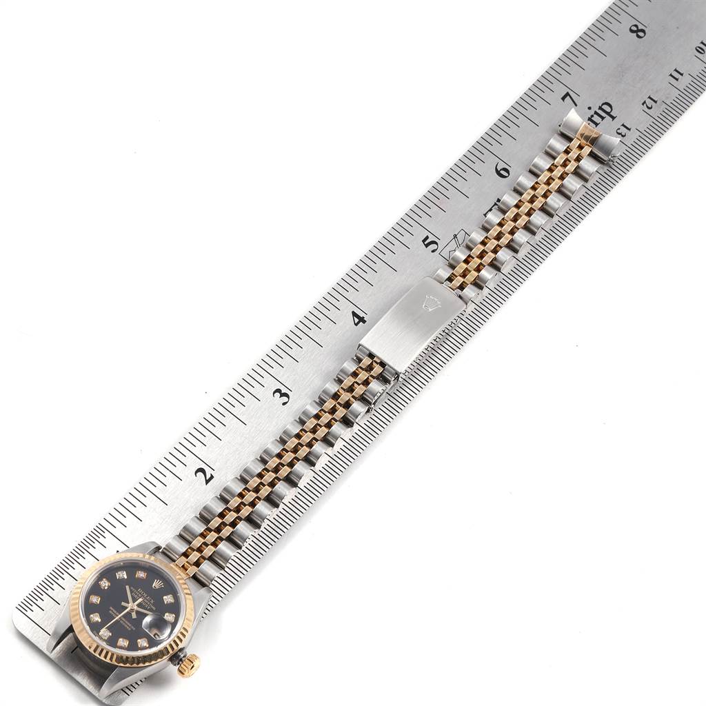 The image shows a Rolex Datejust 79173 Women
s Stainless Steel Black Dial 79173 Women
s Stainless Steel Black Dial watch, including its dial, bezel, and metal bracelet, laid parallel to a ruler.