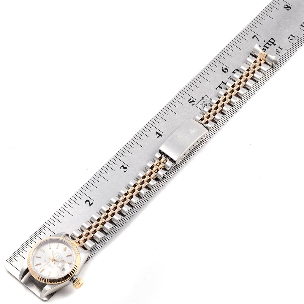 The image shows a Rolex Datejust 79173 Women's Steel and Gold (two tone) Silver Dial 79173 Women's Steel and Gold (two tone) Silver Dial watch laid flat on a ruler, displaying its face and two-tone bracelet with clasp.