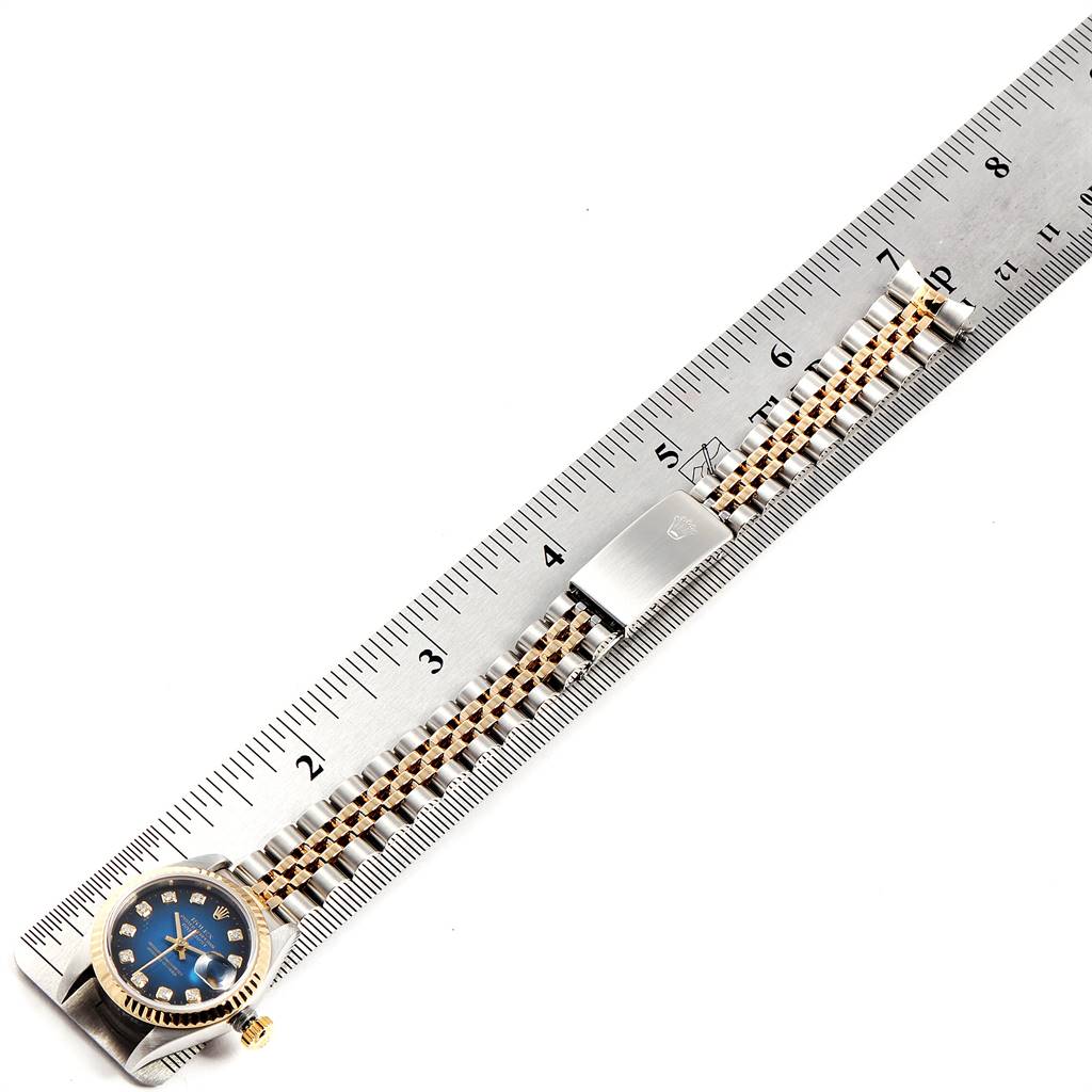 This image shows a Rolex Datejust 79173 Women
s Steel and Gold (two tone) Blue Dial 79173 Women
s Steel and Gold (two tone) Blue Dial watch laid flat next to a ruler, highlighting its band and clasp.