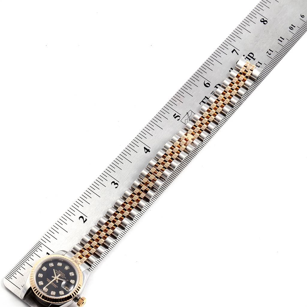 This image shows the face and band of a Rolex Datejust 179173 Women
s Steel and Gold (two tone) Black Dial 179173 Women
s Steel and Gold (two tone) Black Dial watch placed on a metal ruler for measurement.
