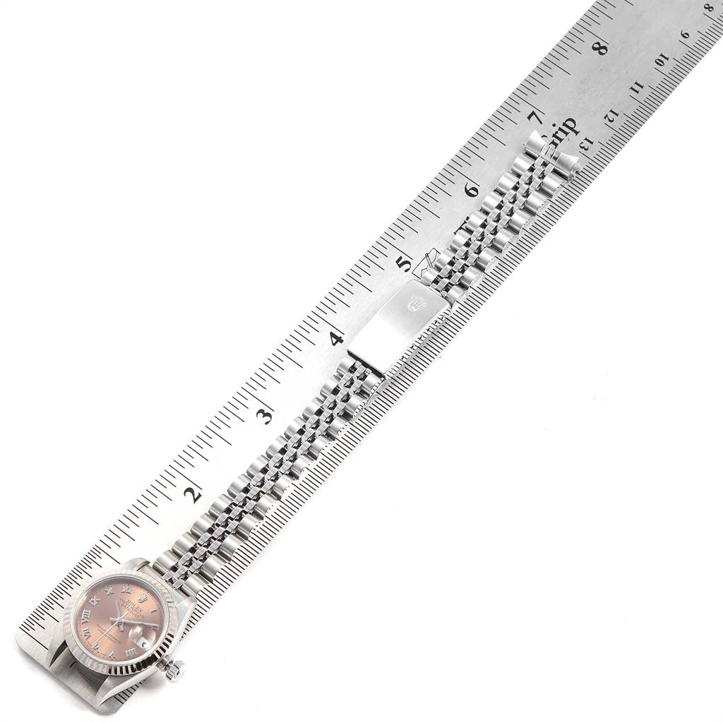 The Rolex Datejust 69174 Women's Stainless Steel Pink Dial 69174 Women's Stainless Steel Pink Dial watch is shown from a top-down angle alongside a metal ruler, displaying the face and bracelet.