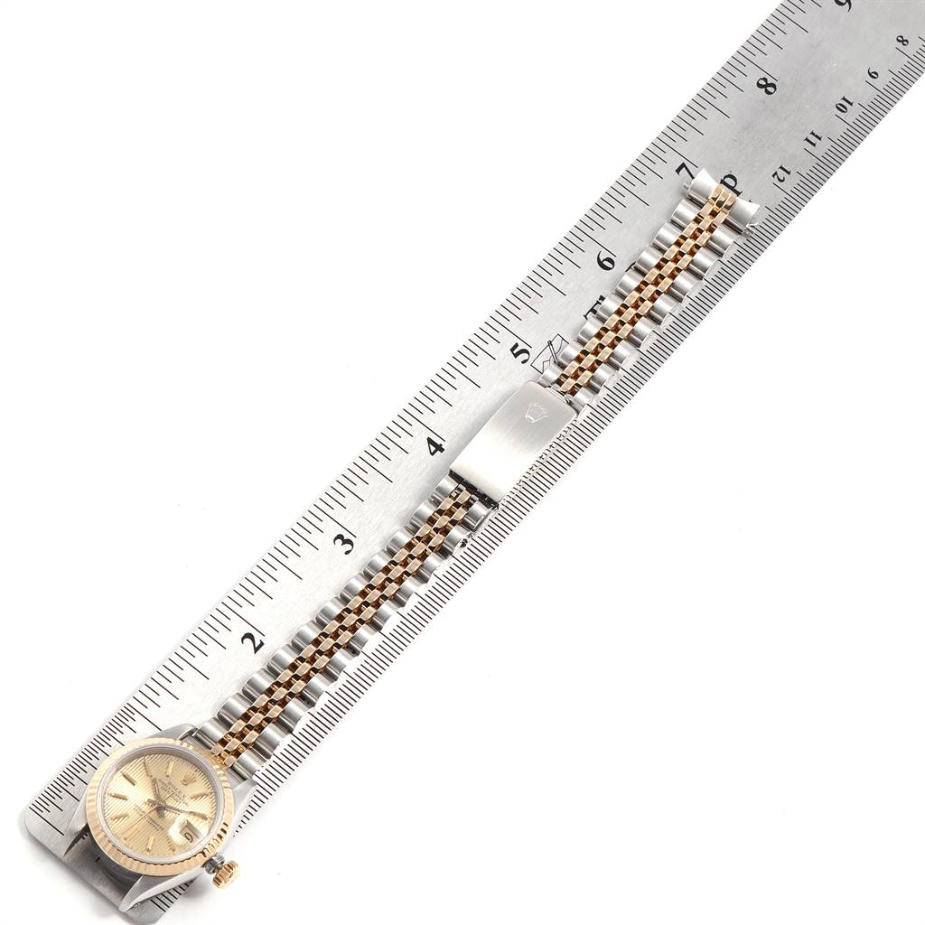 The Rolex Datejust 69173 Women's Stainless Steel Champagne Dial 69173 Women's Stainless Steel Champagne Dial watch is shown from above, featuring the face, crown, and part of the band against a ruler for scale.