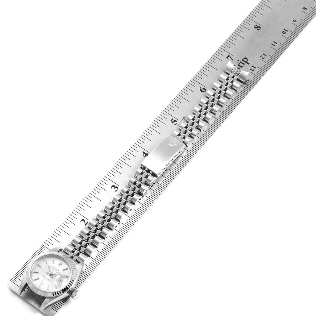 The Rolex Datejust 79174 Women's Stainless Steel Silver Dial 79174 Women's Stainless Steel Silver Dial watch is shown from a top-down angle, displaying its face, bracelet, and clasp placed along a ruler.