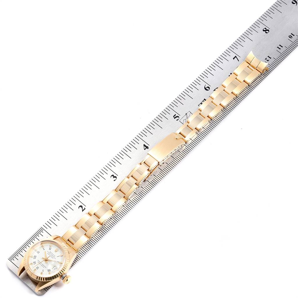 The image shows a Rolex Datejust 6917 Women
s Yellow Gold White Dial 6917 Women
s Yellow Gold White Dial watch laid flat against a ruler, displaying the entire band and face from a top-down angle.