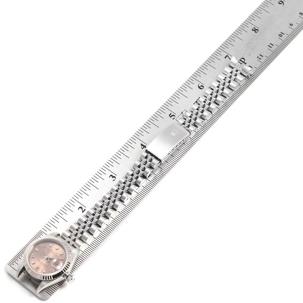 The Rolex Datejust 79174 Women's Stainless Steel Pink Dial 79174 Women's Stainless Steel Pink Dial watch is shown from a top-down angle, highlighting the face and metal bracelet laid along a ruler.