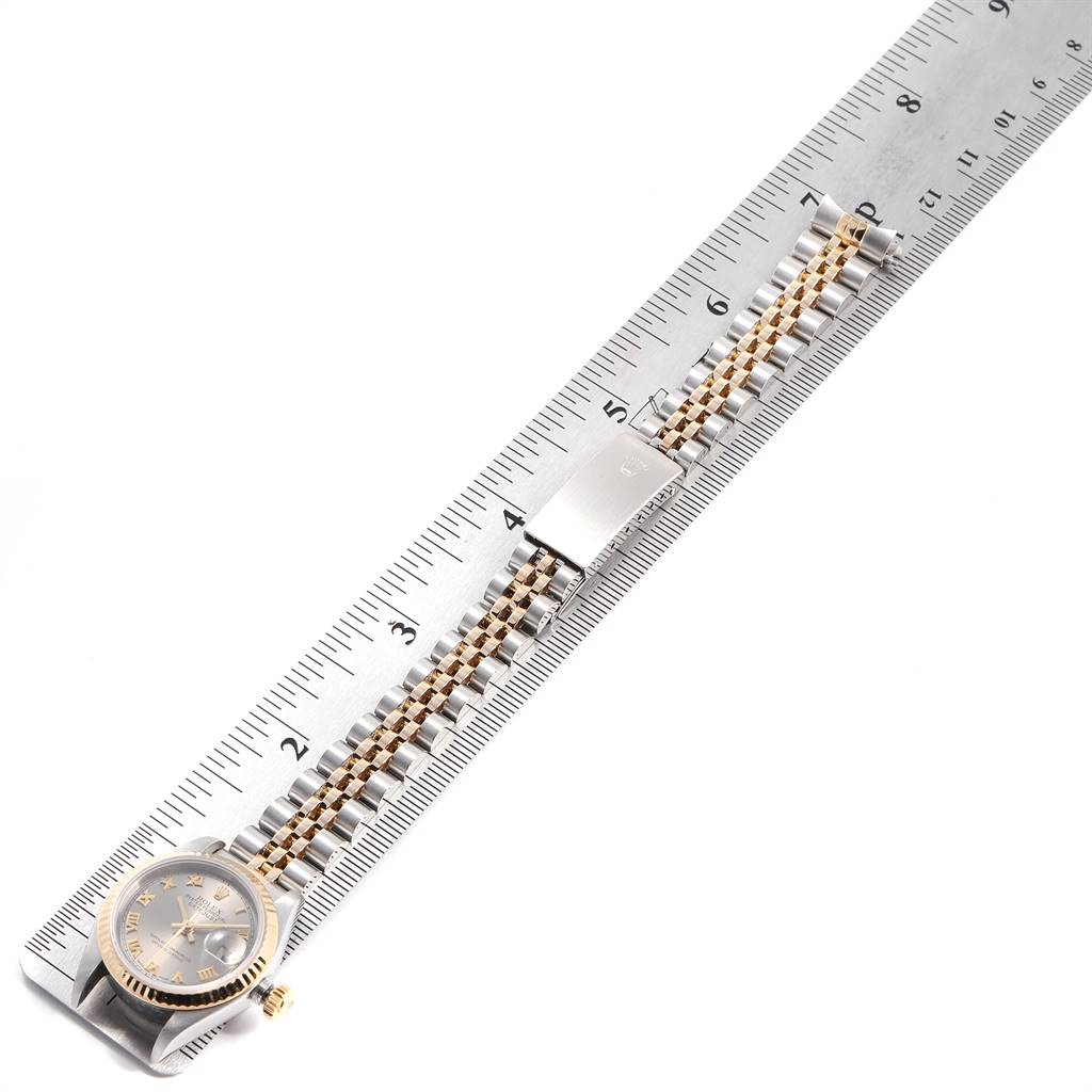 The Rolex Datejust 79173 Women
s Steel and Gold (two tone) Grey Dial 79173 Women
s Steel and Gold (two tone) Grey Dial watch is shown laid flat on a ruler, displaying the face, bracelet, and clasp.