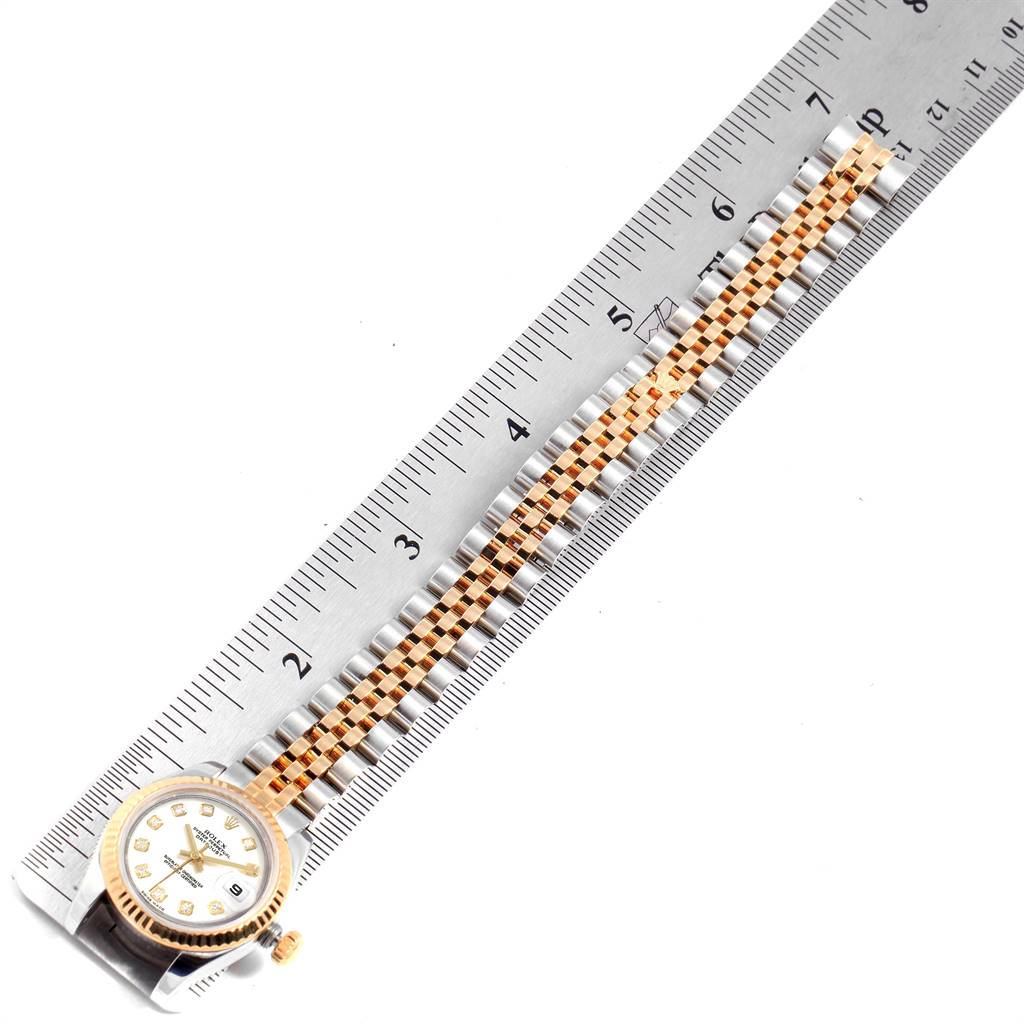 This image shows a Rolex Datejust 179173 Women's Steel and Gold (two tone) White Dial 179173 Women's Steel and Gold (two tone) White Dial watch laid flat on a ruler, showcasing its face and bracelet.