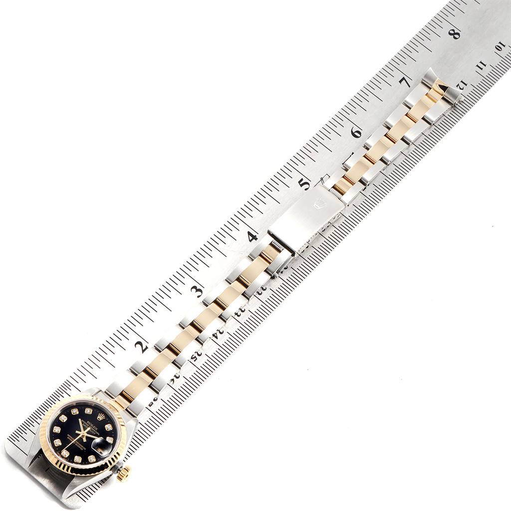 The image shows a Rolex Datejust 79173 Women's Steel and Gold (two tone) Black Dial 79173 Women's Steel and Gold (two tone) Black Dial watch alongside a ruler, displaying its bracelet and dial at a top-down angle.