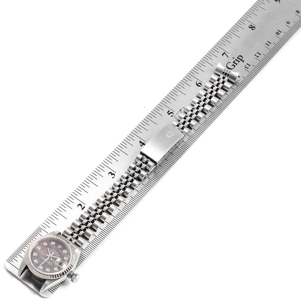 The image shows a Rolex Datejust 79174 Women
s Stainless Steel Mother of Pearl Dial 79174 Women
s Stainless Steel Mother of Pearl Dial watch with an angled view of the face, bracelet, and clasp next to a ruler.
