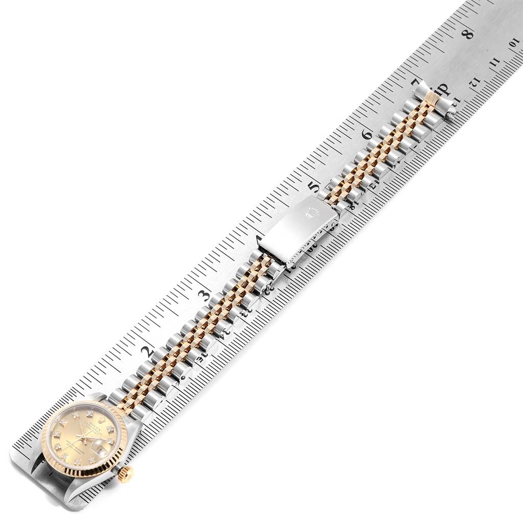 The image shows a Rolex Datejust 69173 Women
s Stainless Steel Champagne Dial 69173 Women
s Stainless Steel Champagne Dial watch laid flat next to a ruler, highlighting its gold dial, bezel, and two-tone metal bracelet.