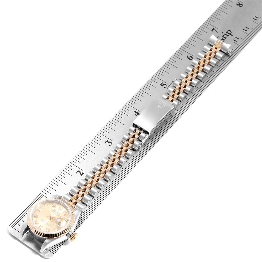 The Rolex Datejust 69173 Women's Stainless Steel Champagne Dial 69173 Women's Stainless Steel Champagne Dial watch is shown laying on a ruler, highlighting its face, band, and clasp from a top-down angle.